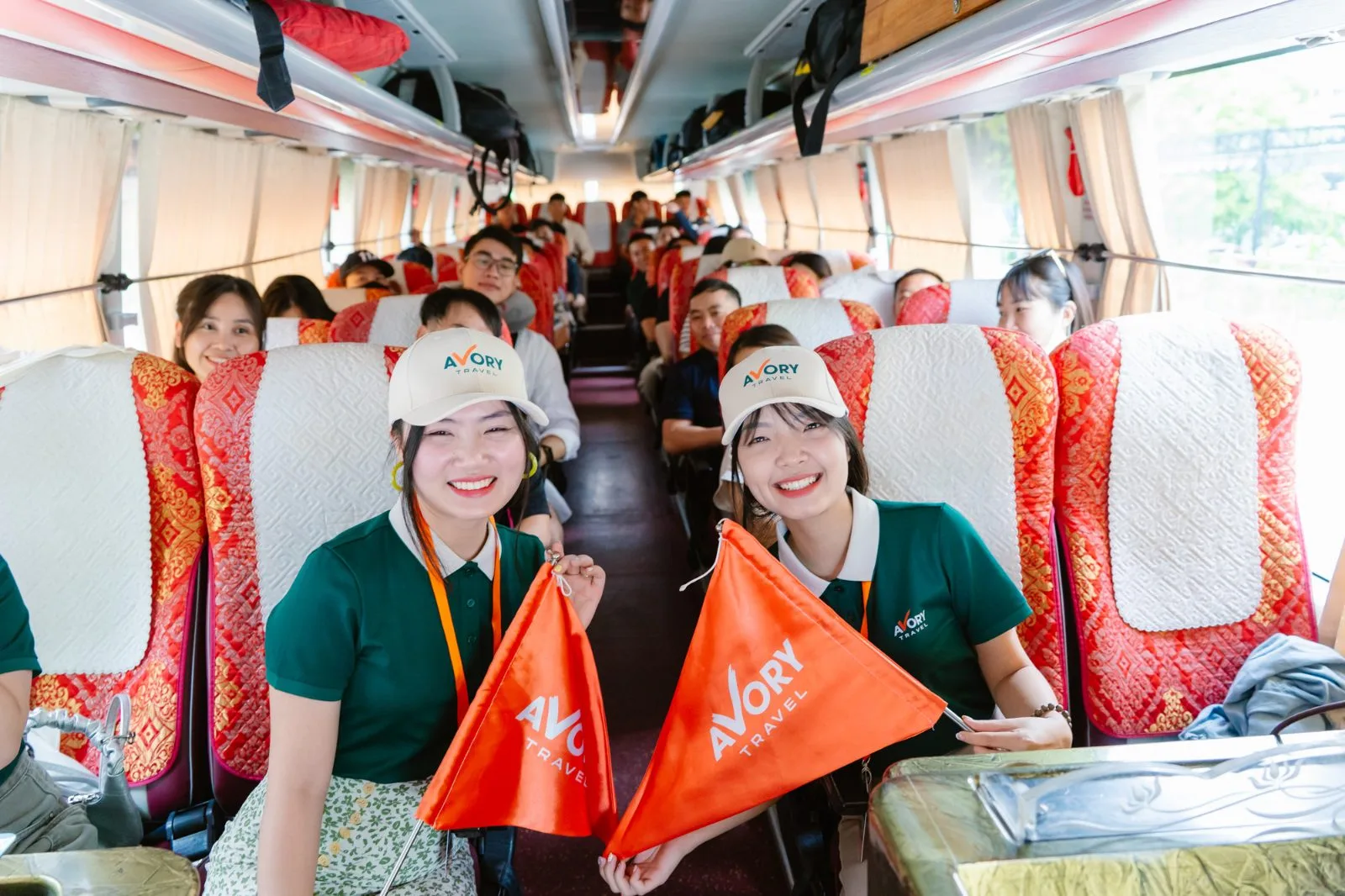Hai hướng dẫn viên Avory cầm cờ trên xe khách, đoàn chuẩn bị khởi hành